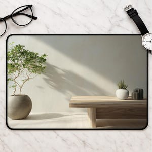 May include: A rectangular desk mat featuring a printed image of a light wood table, a potted green plant in a round grey vase, and a small succulent in a white pot. The mat has a thin black border and is displayed on a white marble surface.