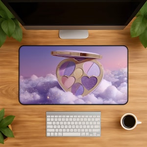 Op de afbeelding: Een rechthoekige bureaumat met een hartvormig make-uppalet met diverse tinten oogschaduw in paars, roze en goud. Het palet is geplaatst tegen een achtergrond van zachte, pluizige wolken in tinten lavendel en roze met gouden sprankelingen.