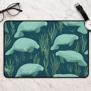 May include: A rectangular desk mat featuring a repeating pattern of light mint green manatees swimming among tall, thin green seagrass on a dark teal background. The mat has a black border and a smooth surface for computer mouse navigation.