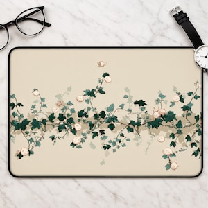 May include: A rectangular desk mat featuring a cream-colored background with a horizontal illustration of dark green ivy vines and small, round, pale pink creatures with simple facial features interspersed among the leaves and stems.