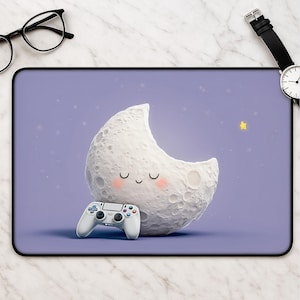 May include: A rectangular mouse mat featuring a light purple background with a white crescent moon character holding a white video game controller. The moon has a smiling face with closed eyes and pink cheeks, set against a starry night sky.