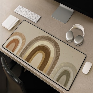 May include: A rectangular desk mat featuring a series of arched rainbow shapes in shades of beige, tan, brown, and muted green. The design includes subtle gold-toned speckles scattered across the background and within the rainbow arches.