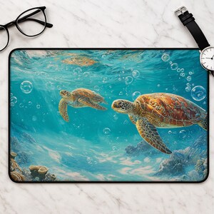 Puede incluir: Una alfombrilla de escritorio rectangular con una escena submarina de dos tortugas marinas nadando entre burbujas y arrecifes de coral. El diseño muestra tonos de agua turquesa y azul, con patrones detallados en marrón y bronceado en los caparazones.