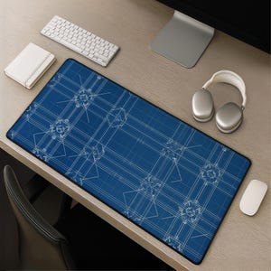 Op de afbeelding: Een rechthoekige bureaumat met een diepblauwe achtergrond en een wit technisch blauwdrukpatroon van geometrische lijnen en mechanische schema's. De mat heeft een zwarte gestikte rand en ligt op een licht houten oppervlak.