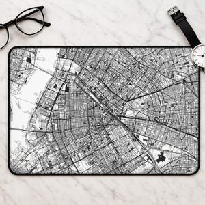 May include: A rectangular desk mat featuring a detailed black and white street map print of a city grid. The mat has a solid black border and displays a complex network of roads, blocks, and waterways in high contrast, providing a clear view.