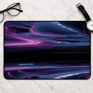 Könnte beinhalten: Eine rechteckige Schreibtischunterlage mit einem dunklen, abstrakten Design aus geschwungenen, verschwommenen Lichtspuren in tiefem Blau und leuchtendem Magenta. Die Oberfläche ist glatt und hat ein schwarzes Querband in der Mitte.