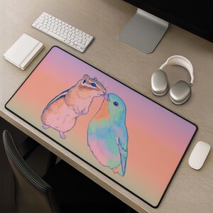 May include: A rectangular mouse pad featuring a colorful illustration of a chipmunk kissing a blue bird. The background transitions from pink to orange. A white keyboard, mouse, and headphones are also visible.