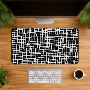 Könnte beinhalten: Eine rechteckige Schreibtischunterlage mit einem kontrastreichen schwarz-weißen Gittermuster. Das Design besteht aus sich kreuzenden horizontalen und vertikalen Linien unterschiedlicher Länge und Abstände, die ein unregelmäßiges, labyrinthartiges geometrisches Motiv bilden.