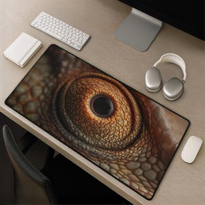 May include: A rectangular desk mat featuring a high-resolution, close-up print of a reptile eye with textured, golden-brown scales surrounding a dark, circular pupil. The mat has a black border and is positioned on a wooden desk surface.