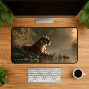 Peut inclure: Un tapis de bureau rectangulaire présentant une impression haute résolution d'un tigre se reposant au bord d'une rivière. Le tigre a des rayures orange et noires et est positionné de profil, tourné vers la droite, parmi un feuillage vert luxuriant.