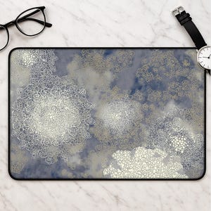 Puede incluir: Una alfombrilla de escritorio rectangular con un fondo azul oscuro nublado de estilo acuarela, superpuesto con intrincados patrones circulares de mandala de encaje blanco y diseños florales de líneas dispersas con un borde negro.