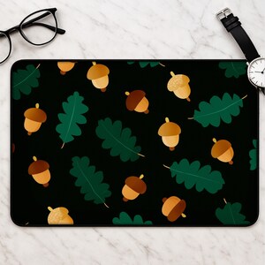 May include: A rectangular desk mat featuring a repeating pattern of brown acorns and dark green oak leaves on a solid black background. The design is flat and graphic, showcasing stylized illustrations of autumn-themed botanical elements.