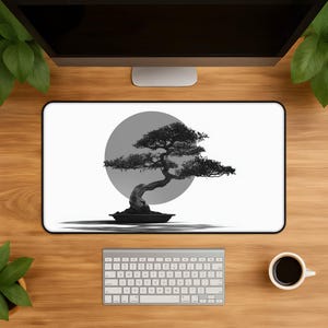 May include: A rectangular desk mat featuring a black and white graphic of a bonsai tree centered in front of a large gray circle. The design is printed on a white background with a thin black border, creating a high-contrast visual display.