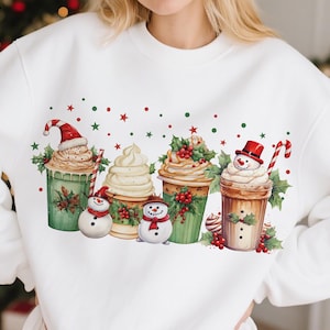 Puede incluir: Sudadera blanca con un diseño festivo de cuatro bebidas navideñas, cada una adornada con crema batida, acebo y un muñeco de nieve. Estrellas y puntos rojos y verdes completan el diseño, ideal para la temporada navideña.