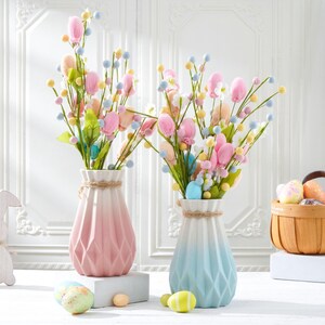 May include: Two decorative vases with floral arrangements, featuring pink and blue ombre tones, are displayed. A wooden bunny and a basket with Easter eggs are also present. The vases have a geometric design and are tied with twine.