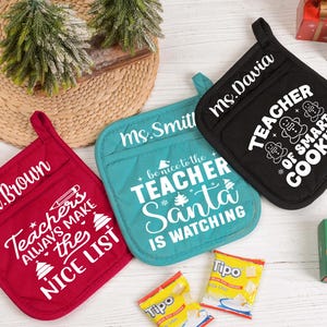 Op de afbeelding: Drie ovenwanten in rood, teal en zwart, elk met een andere boodschap over leraren in het wit. De rode want zegt "Mr. Brown" en "Teachers Always Make the Nice List". De teal want zegt "Ms. Smith" en "Be Nice to the Teacher, Santa is Watching". De zwarte want zegt "Ms. Davia" en "Teacher of Smart Cookies."