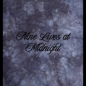 May include: A piece of fabric with a dark gray and black mottled tie-dye pattern. The text 'Nine Lives at Midnight' is printed in a black cursive script across the center of the fabric, which features a visible woven texture throughout the surface.