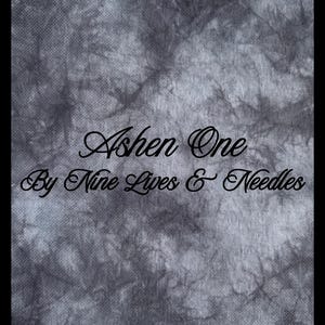 May include: A fabric with a dark gray and black tie-dye pattern. The text Ashen One By Nine Lives & Needles is printed in black in a cursive script font across the center of the fabric, which features a visible woven texture throughout.