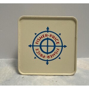 May include: A square, off-white plastic container lid featuring a central blue compass-style graphic. The text FISHER-PRICE is printed in red within the circular blue design, which includes four cardinal direction arrows pointing outward from the center.