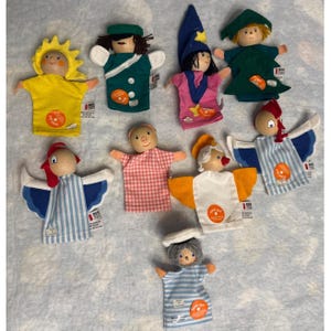 May include: A collection of handmade finger puppets with wooden heads and fabric bodies. The puppets include characters such as a sun, a pig, an angel, and a wizard. Each puppet has a unique design and color scheme, with attached tags.