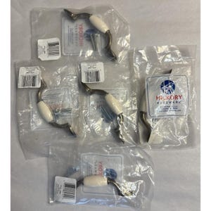 May include: Several cabinet pulls in clear plastic packaging. Each pull has a white ceramic handle, a curved metal base, and includes screws. The packaging includes labels with the "Hickory Hardware" logo and product information.