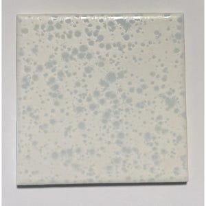 May include: A square ceramic tile featuring a glossy off-white base color with a speckled pattern of light blue and grey dots distributed across the surface. The tile has smooth, straight edges and a reflective finish that catches the light.