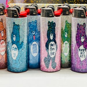 Puede incluir: Una colecci&oacute;n de encendedores cubiertos de purpurina con dise&ntilde;os de Ositos Cari&ntilde;ositos. Cada encendedor tiene un oso diferente y una frase &uacute;nica. Los encendedores son de varios colores, incluyendo azul, rosa, morado y amarillo.