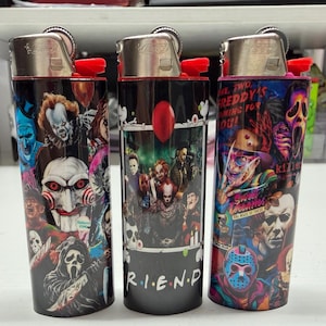 Peut inclure: Trois briquets cylindriques arborant des impressions graphiques color&eacute;es de divers personnages de films d'horreur. Les motifs incluent des figures embl&eacute;matiques comme Pennywise, Billy the Puppet, Ghostface, Freddy Krueger et Jason Voorhees, avec le texte R.I.E.N.D.S.