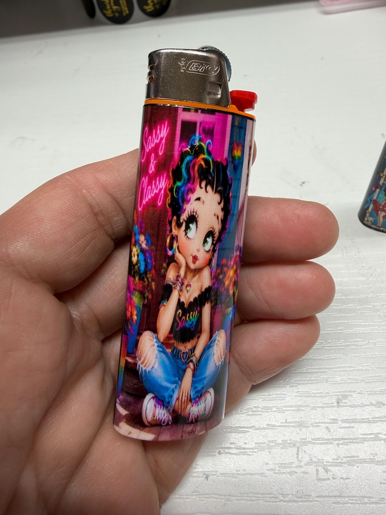 May include: A Bic lighter featuring a colorful graphic of a cartoon character with rainbow-streaked hair, wearing a black off-the-shoulder top and blue jeans. The text Sassy & Classy is printed in pink neon-style script above the character.