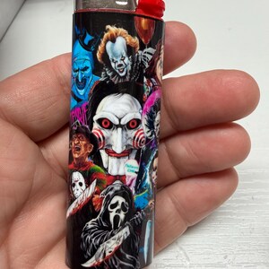 Peut inclure: Un briquet Bic standard dot&eacute; d'un habillage noir orn&eacute; d'un collage de divers personnages de films d'horreur, incluant un masque de marionnette blanc central aux joues en spirale rouge, une silhouette encapuchonn&eacute;e avec un couteau et d'autres figures.