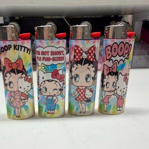 May include: Four cylindrical lighters featuring a colorful tie-dye background and cartoon graphics of Betty Boop and Hello Kitty. The lighters display text including BOOP KITTY, I'M NOT SHORT, I'M FUN-SIZED, and BOOP, with metallic tops.