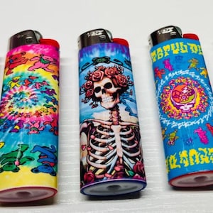 May include: Five colorful lighters with unique designs. One features a skull and cartoon characters, another a tie-dye pattern with dancing bears, and a third a skeleton with roses. The fourth has a circular design, and the last one has a skull and the words "Grateful Dead".