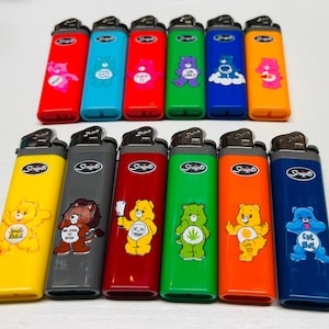 May include: A collection of colorful lighters with various cartoon bear designs. The lighters are in shades of red, blue, green, yellow, orange, and gray. Each lighter has a different bear graphic and the word "Scripto" printed on the side.