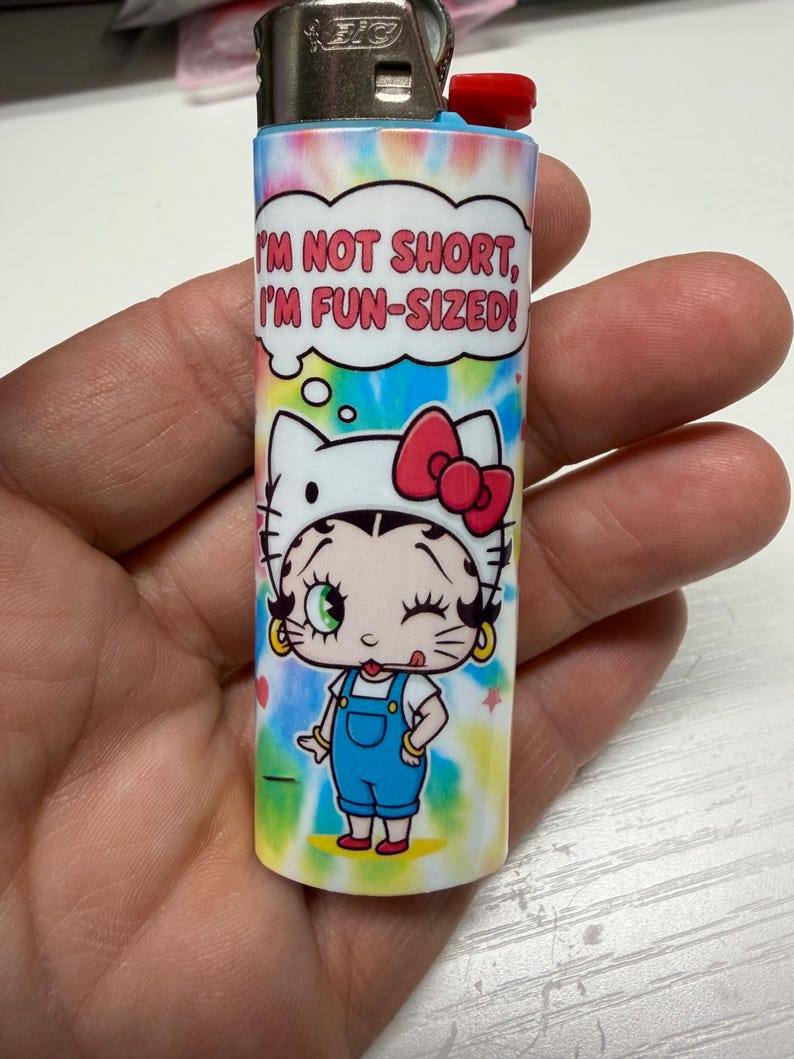 May include: A Bic lighter featuring a tie-dye background and a graphic of a character wearing a cat-ear headband with a red bow. Above the character is a speech bubble containing the text, I'M NOT SHORT, I'M FUN-SIZED! in red capital letters.