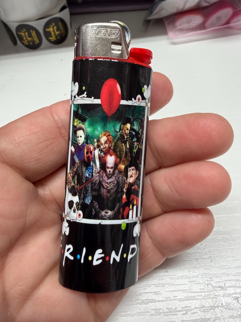 Peut inclure: Un briquet Bic noir orn&eacute; d'une impression graphique repr&eacute;sentant divers personnages de films d'horreur, un ballon rouge et un cr&acirc;ne. Le texte R.I.E.N.D est imprim&eacute; en blanc en bas, avec des points color&eacute;s entre les lettres. Sommet m&eacute;tallique.