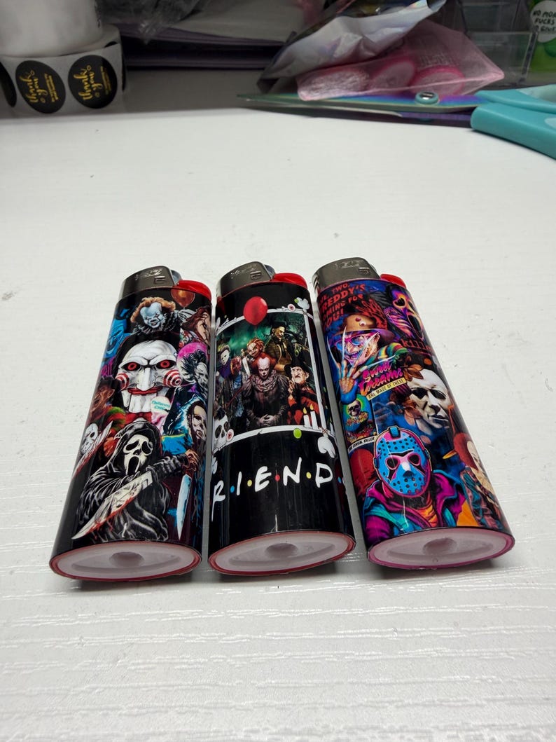 Peut inclure: Trois briquets rectangulaires orn&eacute;s d'impressions graphiques color&eacute;es repr&eacute;sentant divers personnages de films d'horreur. Le briquet central affiche le texte R.I.E.N.D. et un ballon rouge. Les motifs incluent Ghostface, Jigsaw et Jason Voorhees.