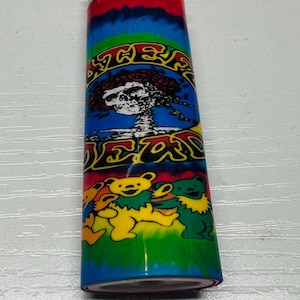 Puede incluir: Un encendedor colorido con un dise&ntilde;o tie-dye en la parte superior y una vibrante ilustraci&oacute;n de una calavera y osos. El encendedor tiene una parte superior de metal y un cuerpo verde, azul y amarillo.