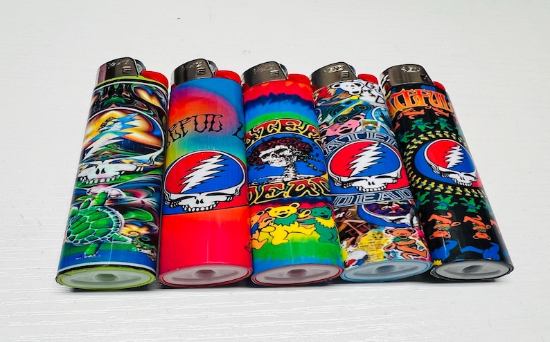 Puede incluir: Cinco encendedores coloridos con varios dise&ntilde;os, incluyendo una tortuga, una calavera con rayos y osos bailarines. Los encendedores tienen botones de encendido rojos y est&aacute;n sobre una superficie blanca.