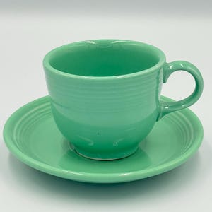 Puede incluir: Un juego de taza y platillo verde menta. La taza tiene forma redondeada con asa, y el platillo es circular. Ambas piezas tienen un diseño acanalado. El juego es de cerámica.