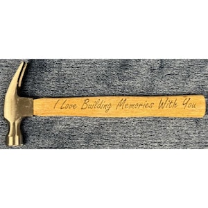 May include: A claw hammer with a wooden handle. The handle is engraved with the phrase "I Love Building Memories With You". The hammer head is silver-colored, and the handle is light brown.
