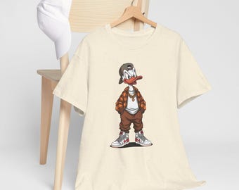 May include: Cream-colored t-shirt featuring a cartoon duck wearing a backwards cap, gold chain, and a brown and orange plaid jacket. The duck is also wearing brown pants and white sneakers with red accents. A white baseball cap rests on a wooden chair.