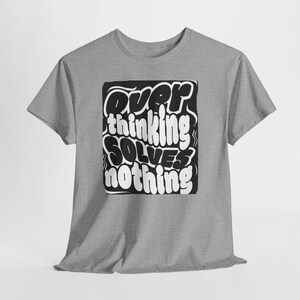 Puede incluir: Una camiseta gris jaspeado con el texto "Overthinking Solves Nothing" en un diseño en blanco y negro. El texto está en negrita, con una fuente estilizada, centrado en la camiseta.