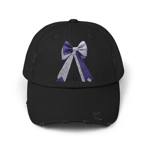 May include: Black distressed baseball cap featuring a purple and white bow design. The bow has a white center and purple ribbon tails with white polka dots. The cap has a curved brim and a distressed finish.