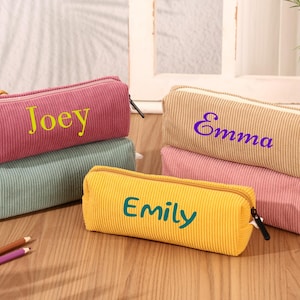 Puede incluir: Estuches de lápices de pana en varios colores, como rosa, beige, amarillo y verde. Cada estuche rectangular tiene cremallera y un nombre bordado: Joey, Emma y Emily. Ideales para guardar útiles escolares.