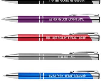 May include: Five ballpoint pens in black, purple, red, gray, and blue. Each pen has silver accents and a different phrase printed on the barrel: "I AM THE FUCKING HR MANAGER!", "AS PER MY LAST FUCKING EMAIL", "DID I JUST ROLL MY EYES OUT LOUD?", "HOW ABOUT NO?", and "I AM SILENTLY JUDGING GRAMMAR".