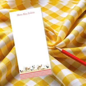 May include: A white notepad with the text "Mary Alice Jenkins" in red at the top. The bottom of the notepad features a watercolor illustration of chickens and a red and white checkered border. A red pencil rests on a yellow and white checkered tablecloth.