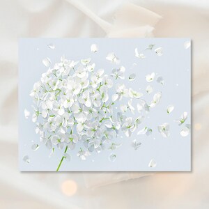 May include: A light blue rectangular print featuring a cluster of white flowers with delicate petals. Some petals are scattered around the floral arrangement, creating a sense of movement. The background is a soft, light blue.