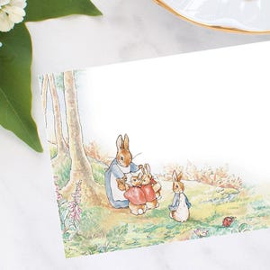 May include: A watercolor illustration of a family of rabbits in a forest setting. The mother rabbit is wearing a blue dress and holding two baby rabbits in her arms. The baby rabbits are wearing red coats. A third baby rabbit is standing behind the mother rabbit. The rabbits are surrounded by green trees and bushes.