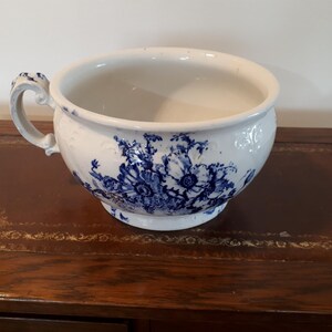 May include: A white ceramic bowl featuring a blue floral design. The bowl has a handle and a pedestal base. The blue floral pattern decorates the exterior, giving it a vintage appearance. The bowl is likely made of ceramic.
