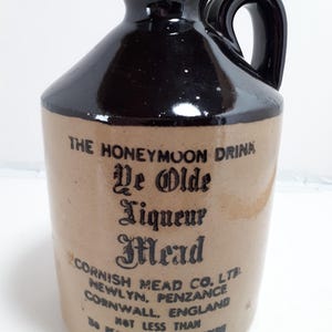 Peut inclure: Une cruche en grès vintage avec un dessus et une poignée émaillés brun foncé et un corps beige. La cruche présente des inscriptions noires qui se lisent "THE HONEYMOON DRINK Ye Olde Liqueur Mead". La cruche est de Cornish Mead Co. Ltd, Angleterre.